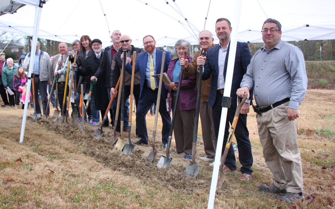 People holding shovels standing under a tent at a groundbreaking ceremony