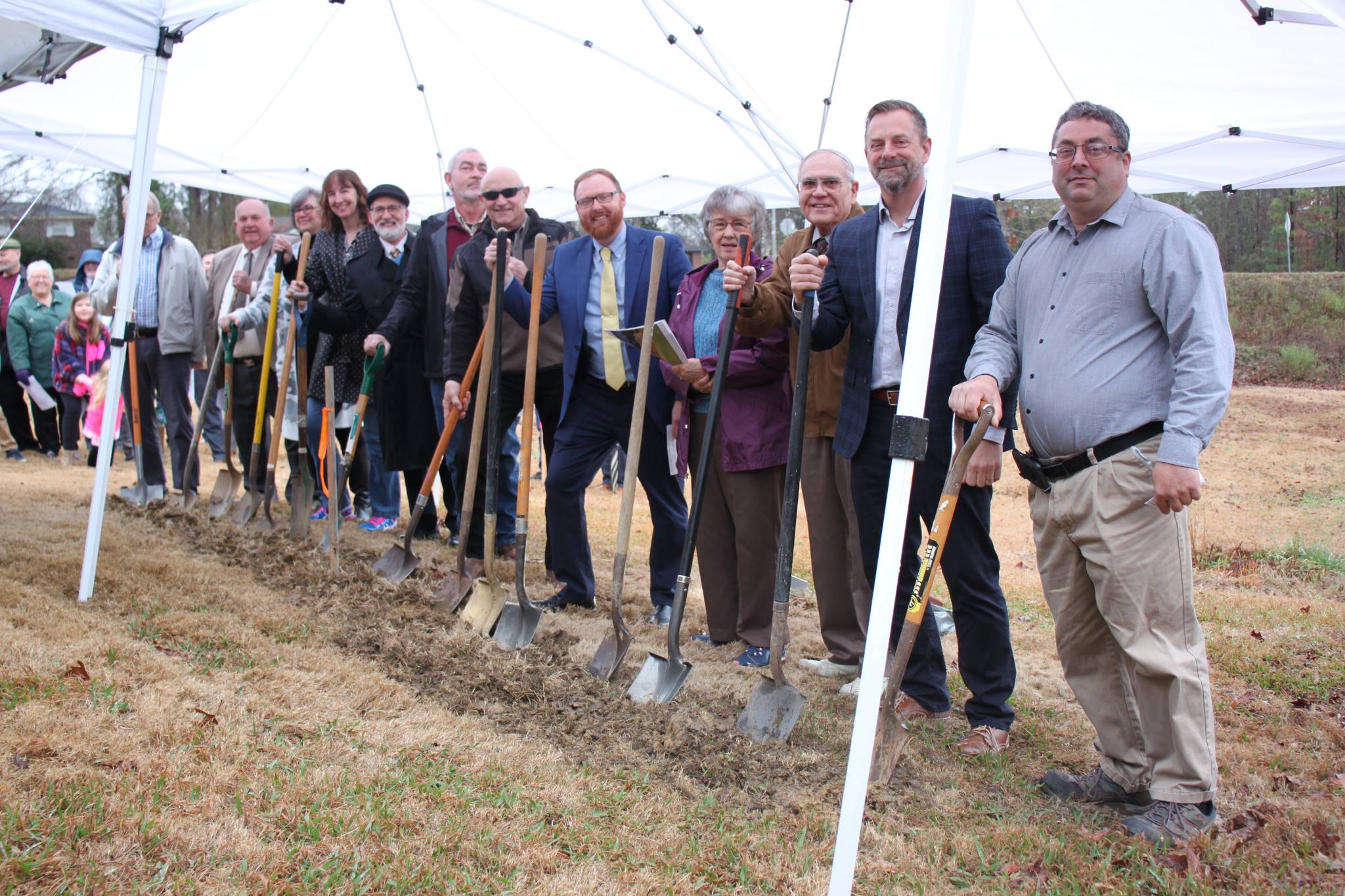 People holding shovels standing under a tent at a groundbreaking ceremony