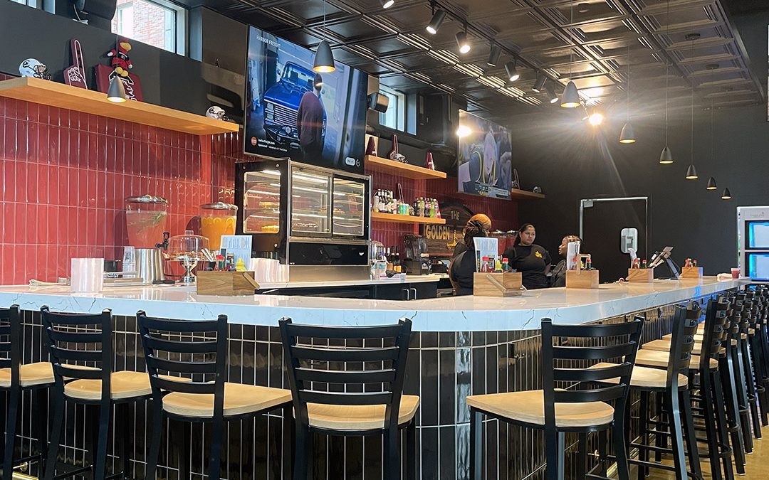 A photo of the bar in the new Golden Spur restaurant on the USC campus. The bar front has vertical black tile and the bar back is garnet. The counter top is quartz and has gold accents.